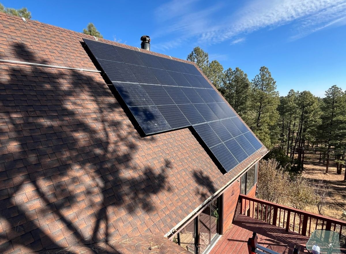 Black bifacial solar panels on the pitched roof of a wood-sided home among tall pines in Flagstaff, Arizona